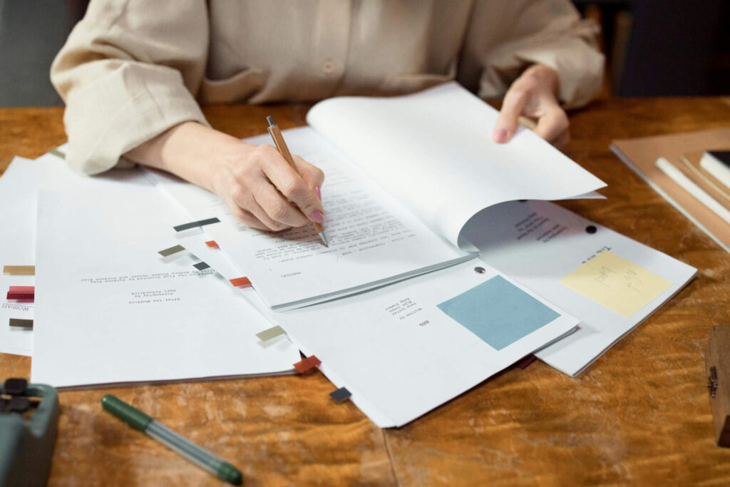 Une personne écrit sur une feuille, sur un bureau jonché de documents.