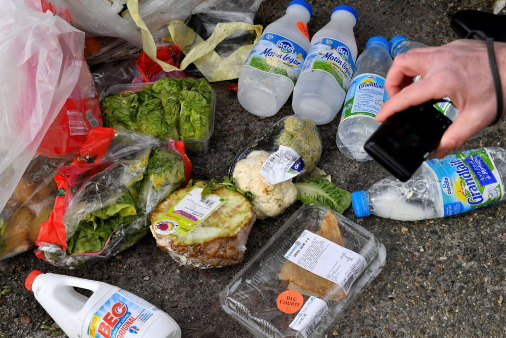 Des produits au sol sortis d’une poubelle, sont photographiés par des membres d’une association.