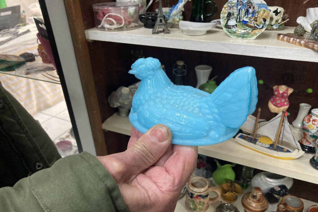 Un client tient une poule bleu ciel faite en opaline.