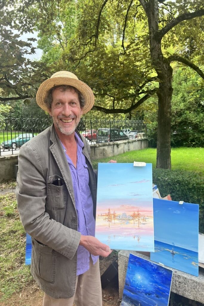 Franck Martin tient dans ses mains le tableau qu’il a réalisé représentant l’Opéra de Vichy dans un monde imaginaire. Il se trouve toujours dans un cadre verdoyant.