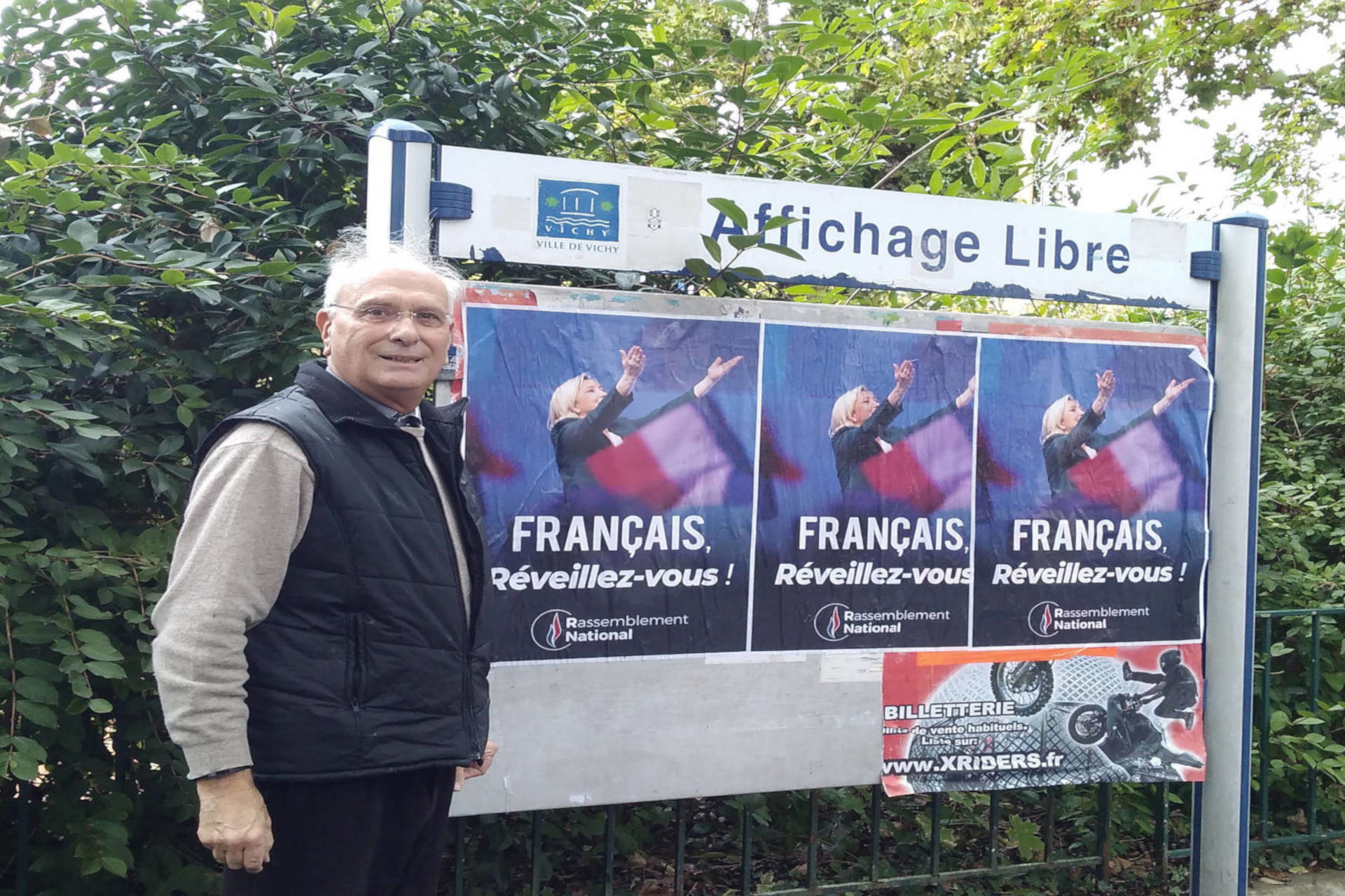 Jean Pierre Sigaud à Vichy pose devant des affiches de campagne RN.