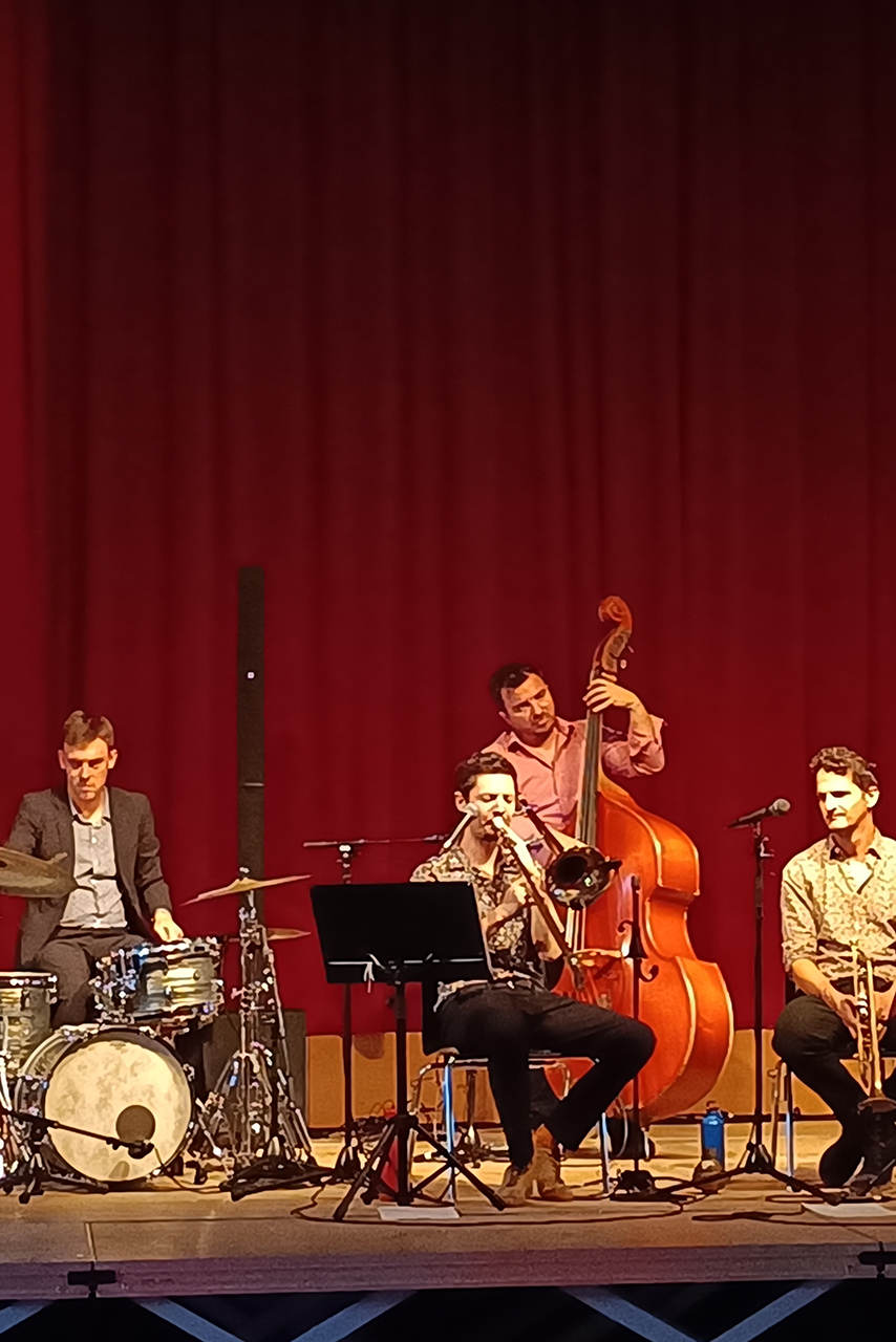 Photo montrant le groupe Woo Katz au festival Vichy Jazzy, le dimanche 20 octobre à 17 h, à la salle des fêtes de Vichy. On y voit 3 hommes assis jouant de leur instrument et un homme debout jouant également de son instrument. Les 4 artistes jouent du Jazz New Orleans sur scène, face à un public assis.
