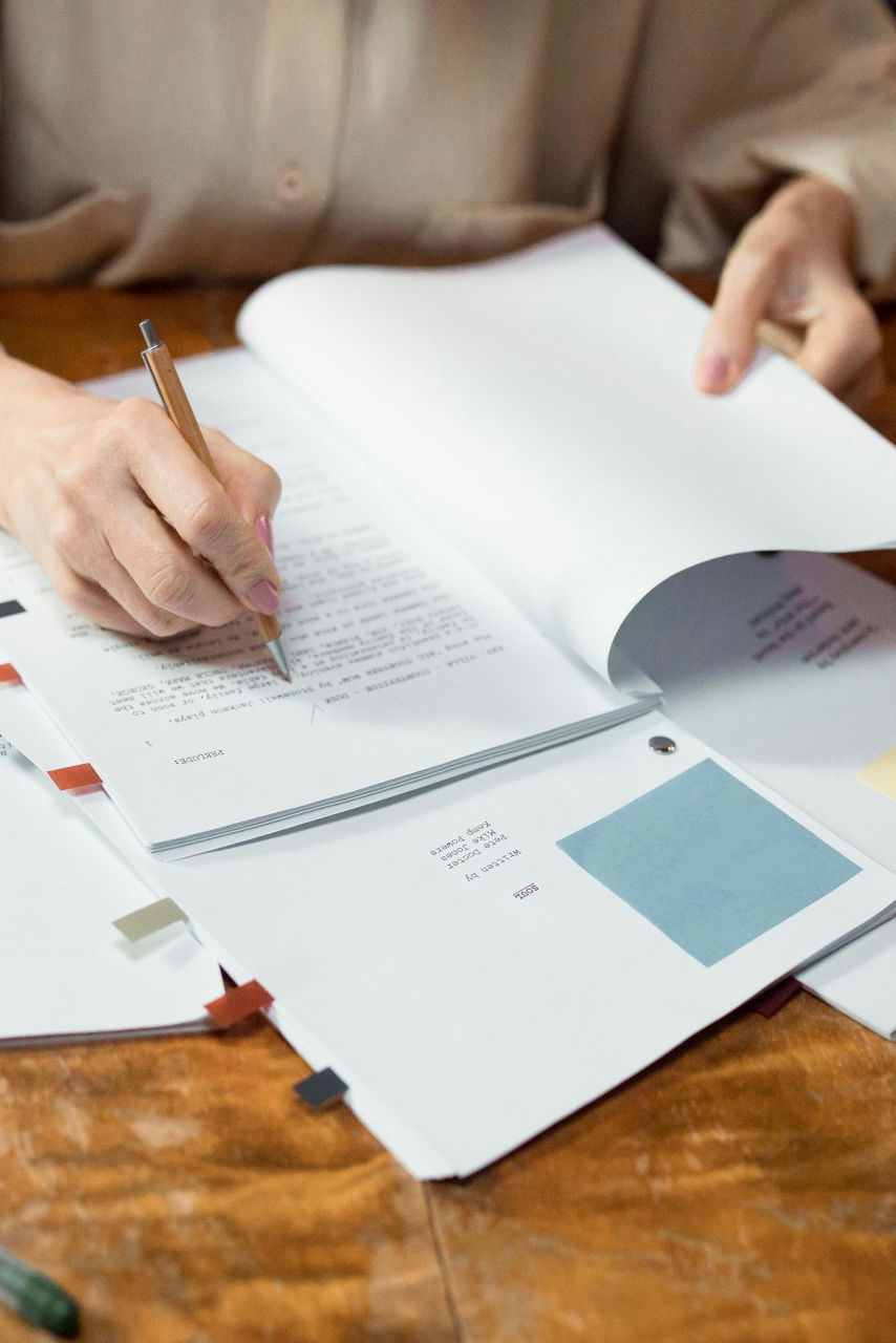 Une personne écrit sur une feuille, sur un bureau jonché de documents.