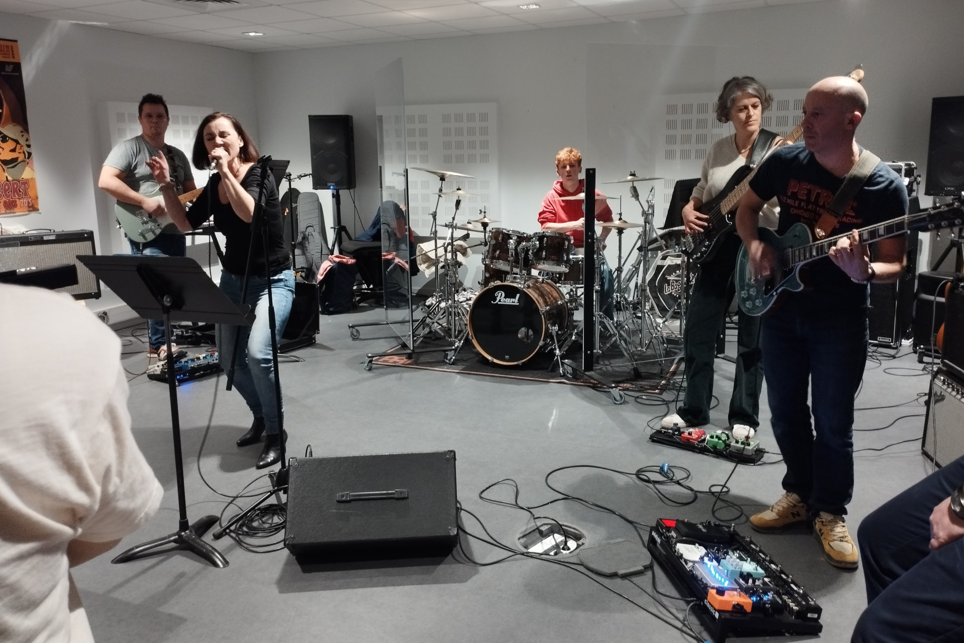 Les adultes du conservatoire jouent dans leur salle de classe : la chanteuse est accompagnée de guitares, basse et batterie.