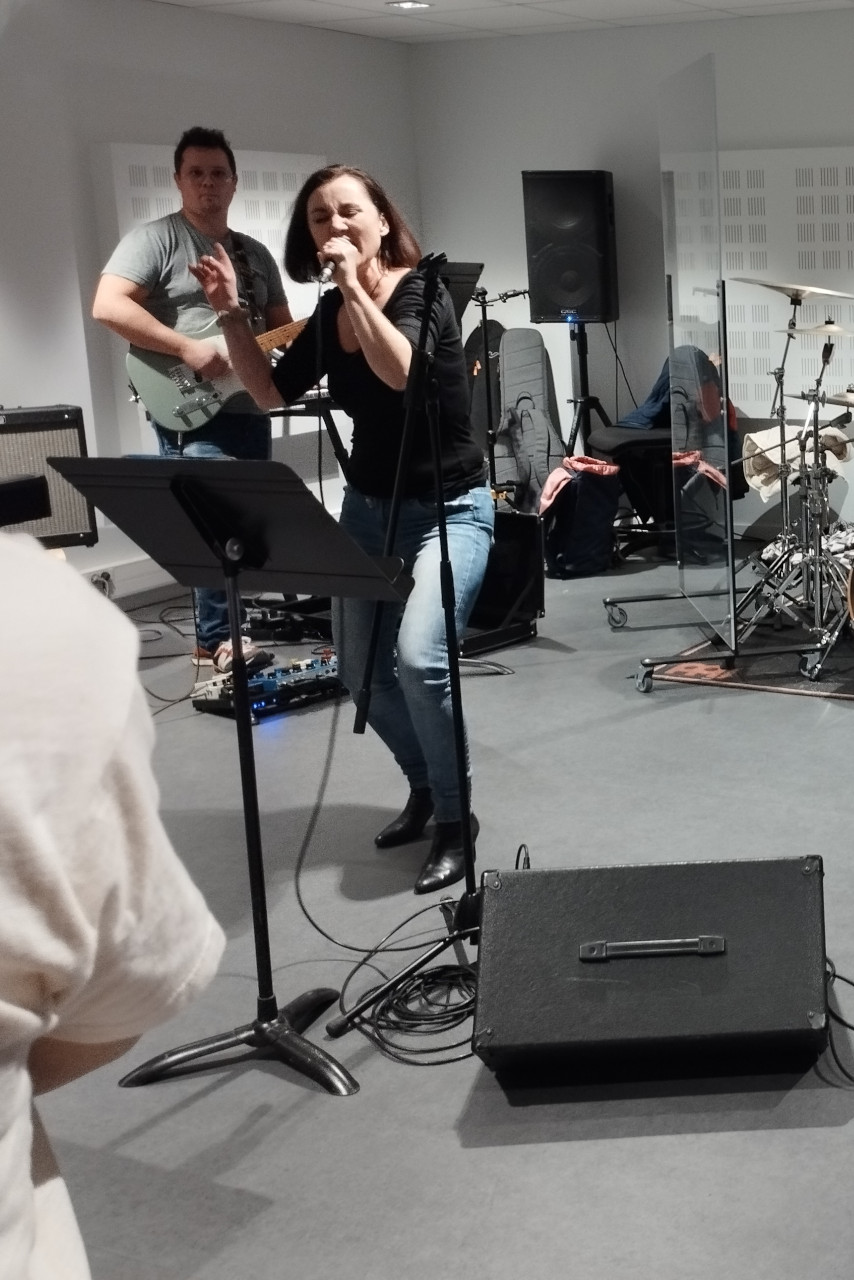 Les adultes du conservatoire jouent dans leur salle de classe : la chanteuse est accompagnée de guitares, basse et batterie.