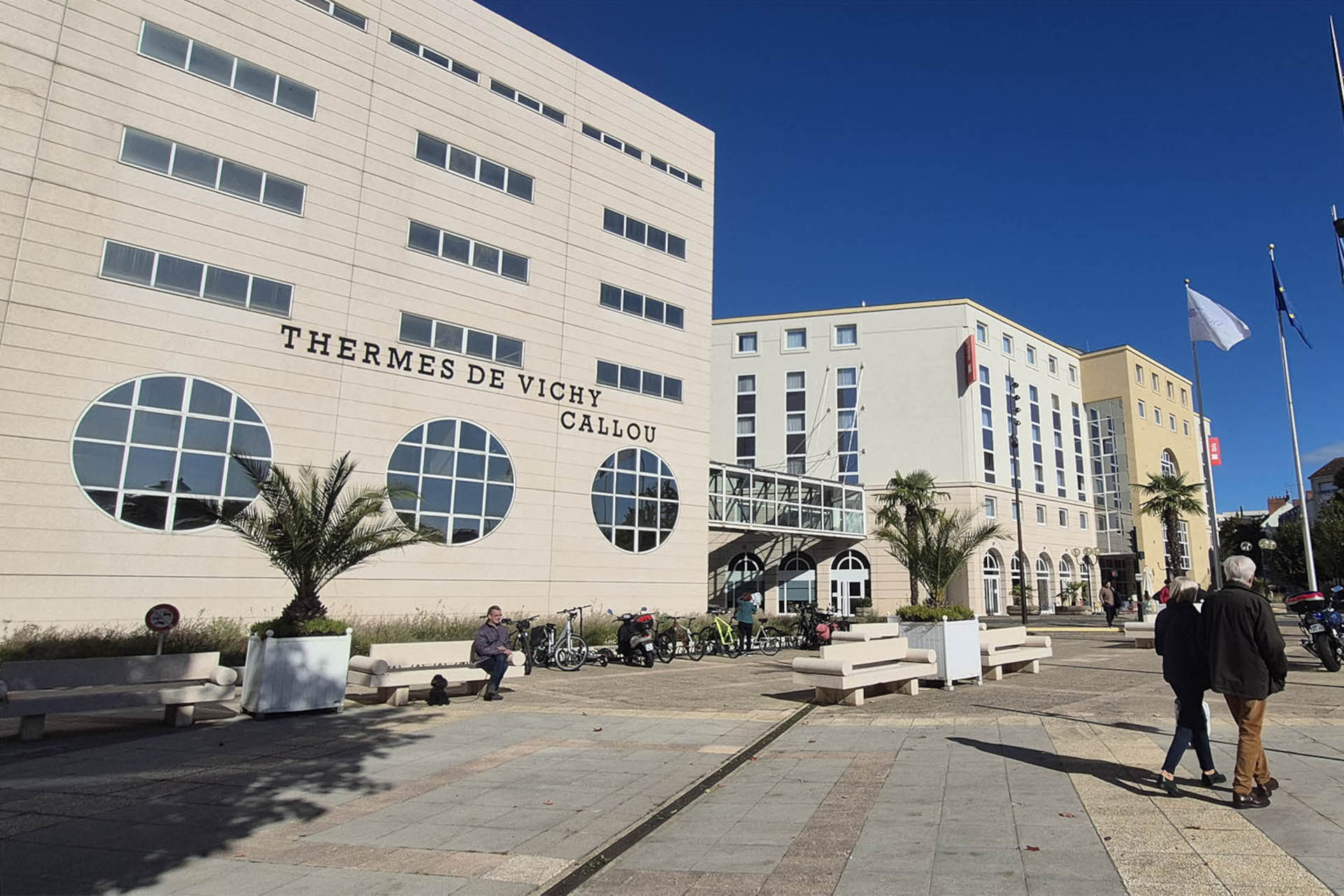 Des passants marchent dos au bâtiment des thermes Calou à Vichy le 3 octobre 2025.