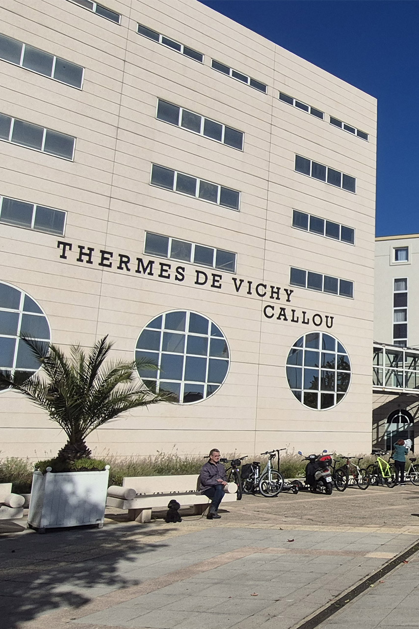 Des passants marchent dos au bâtiment des thermes Calou à Vichy le 3 octobre 2025.