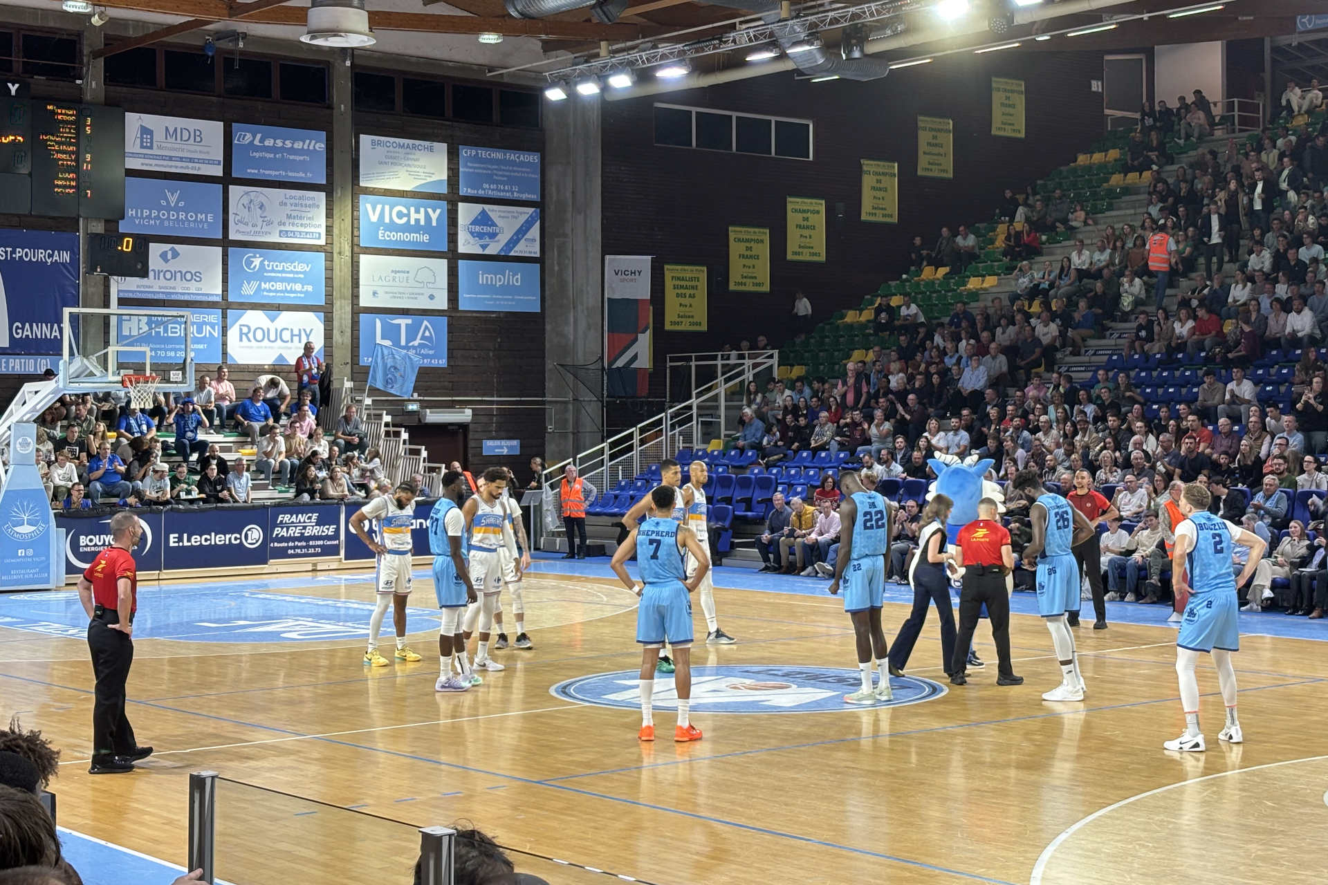 Des joueurs de basket et un arbitre sur le parquet au tout début d'un match.