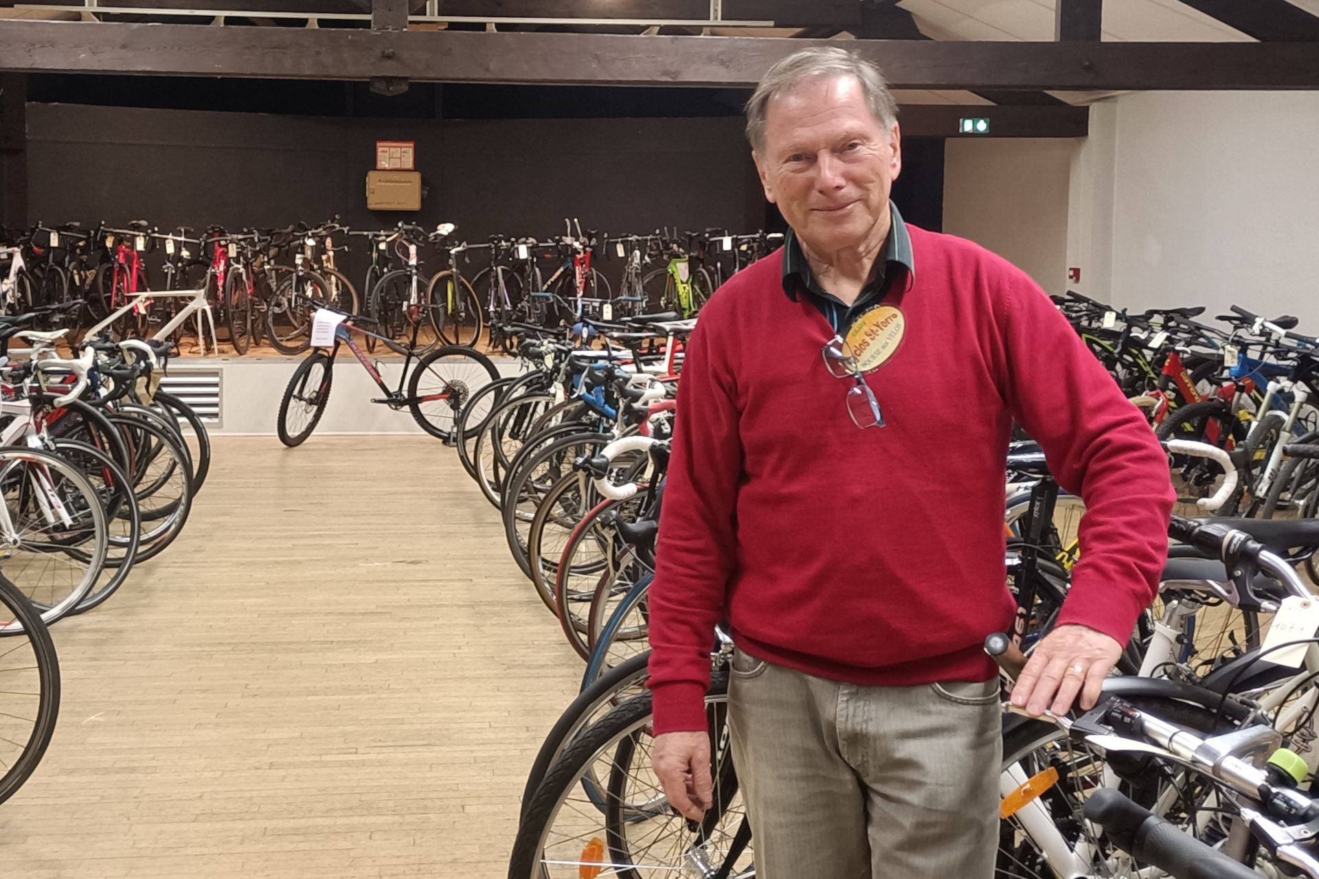 Philippe Derenchy est au centre de l’image et regarde l’objectif. Il est entouré de vélos, stockés dans un hangar.