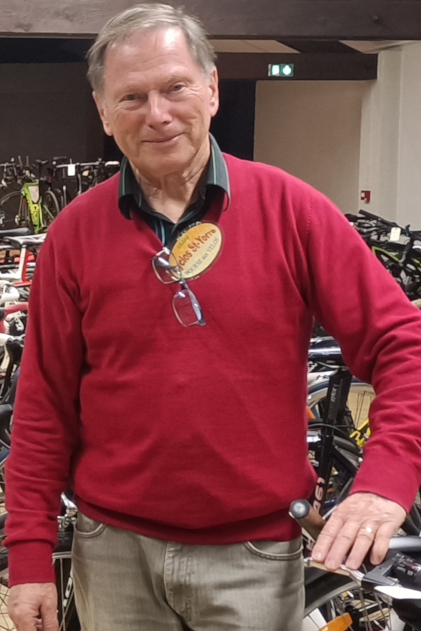 Philippe Derenchy est au centre de l’image et regarde l’objectif. Il est entouré de vélos, stockés dans un hangar.