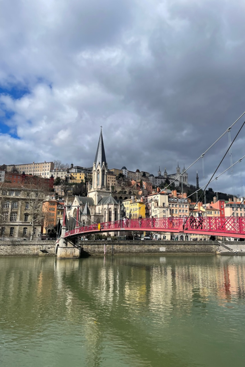 Vue du pont Saint-Georges à Lyon au-dessus de la Saône, avec la colline de Fourvière et ses bâtiments historiques en arrière-plan.